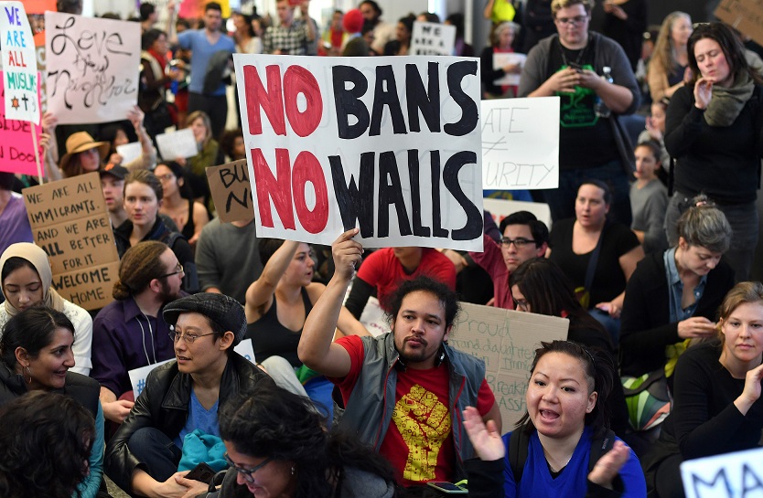 TOPSHOT - Protesters sit in the international terminal at San Francisco International Airport in San Francisco, California on January 29, 2017. US President Donald Trump issued an executive order yesterday barring citizens of seven Muslim-majority countries from entering the United States for the next 90 days and suspends the admission of all refugees for 120 days. / AFP PHOTO / Josh Edelson